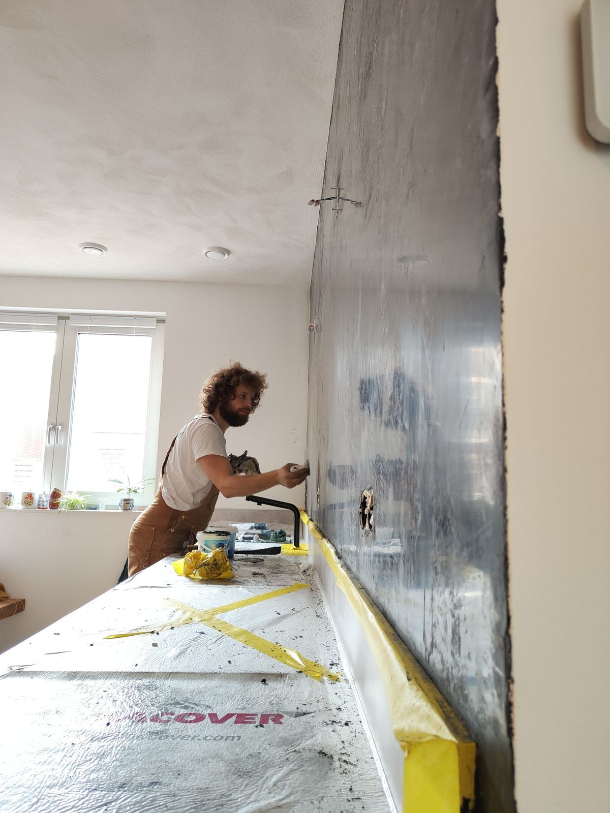 De maker aan het werk aan de antraciet wand, het keukenblad afgedekt
