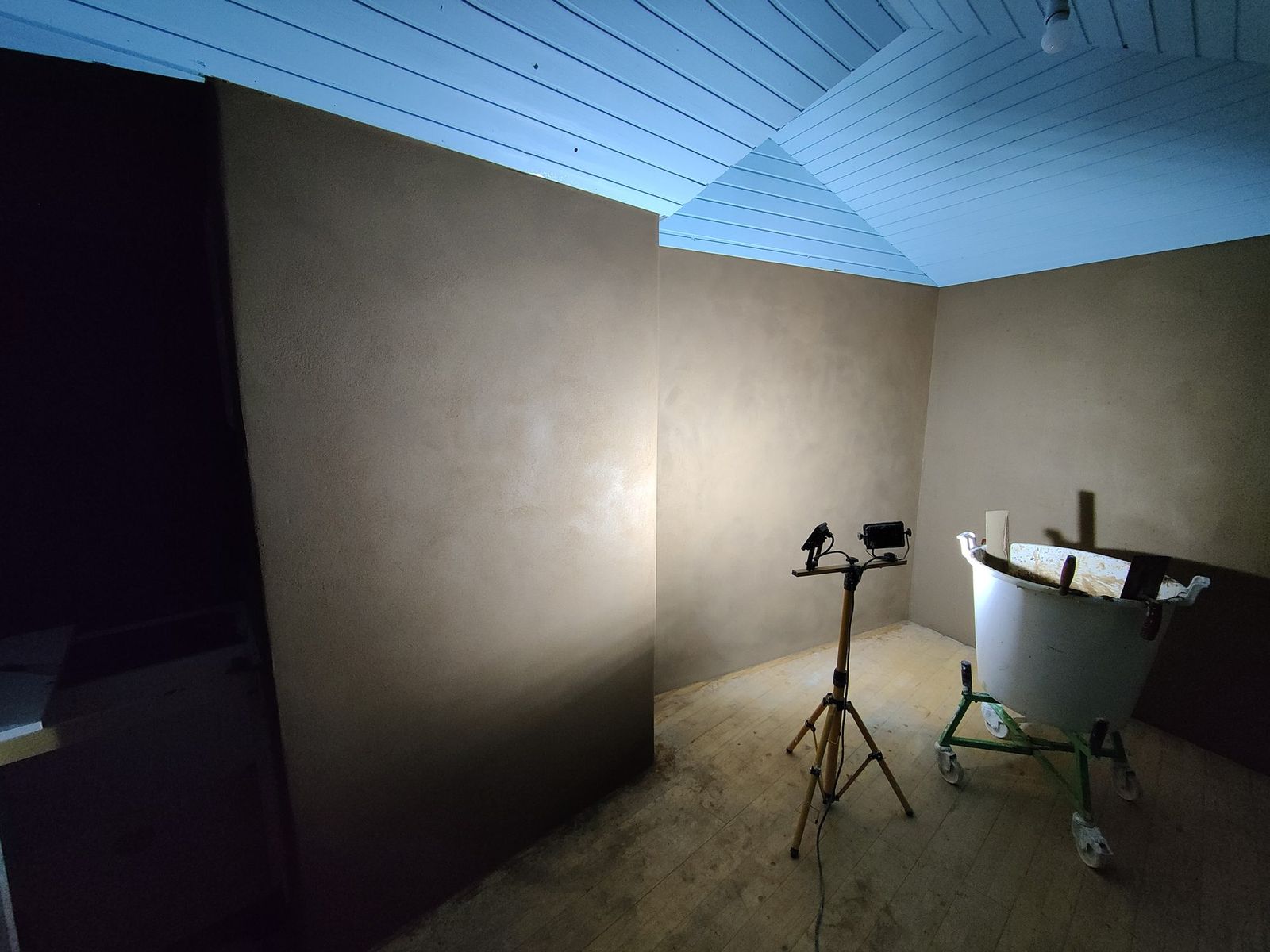 Kamer onder een schuin plafond, wanden zonder pigment in de eigen kleur van de klei, een lamp op statief